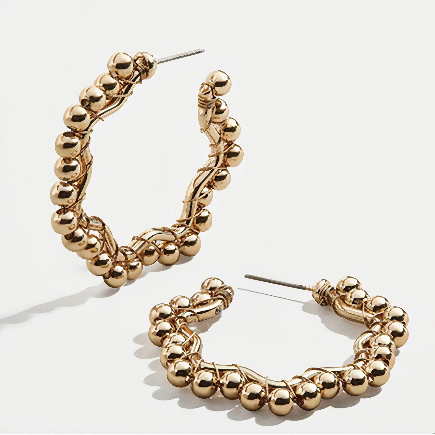 Pair of gold hoop earrings with wrapped wire and polished bead details on white background