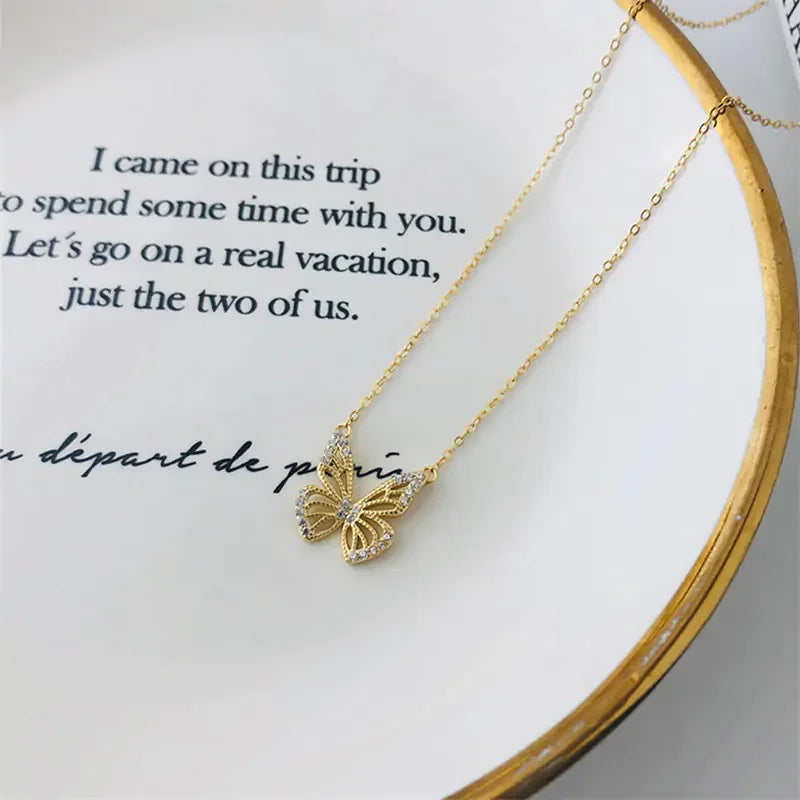 Elegant gold butterfly pendant necklace with crystal accents on a white dish with text, showcasing fine jewelry