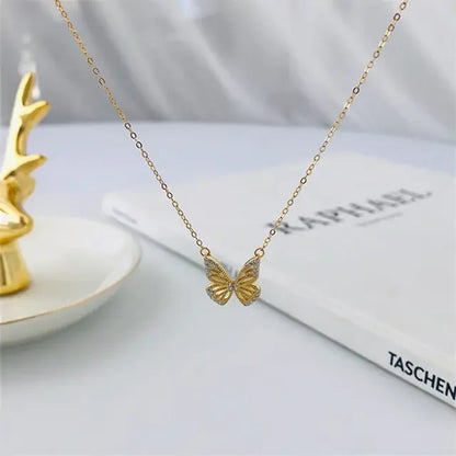 Delicate gold butterfly pendant necklace displayed with a decorative gold antler on a white dish and a TASCHEN book