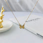 Delicate gold butterfly pendant necklace displayed with a decorative gold antler on a white dish and a TASCHEN book