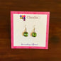 ClaudiaG green gemstone dangle earrings displayed on branded card with pink border on wooden surface