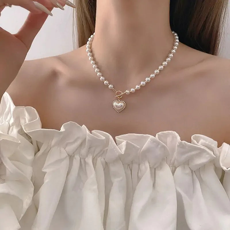 Close-up of a woman wearing a pearl necklace with a gold heart pendant and off-shoulder white ruffled top