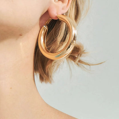 Close-up of a woman's ear wearing a large chunky gold hoop earring with short blonde hair