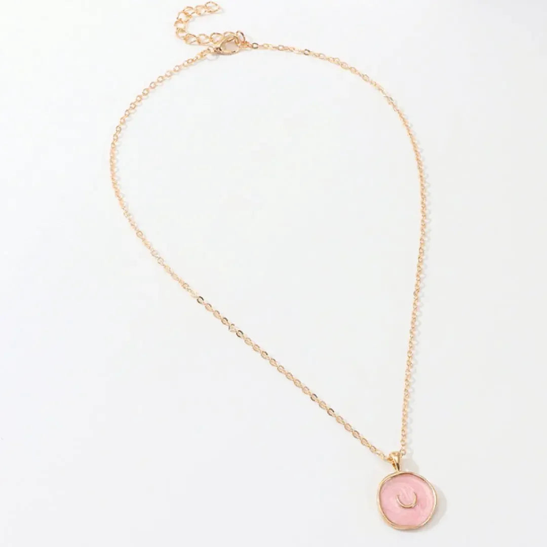 Delicate gold chain necklace with pink circular pendant featuring crescent detail, on white background