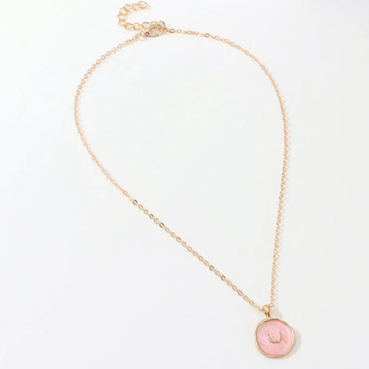 Delicate gold chain necklace with pink circular pendant featuring crescent detail, on white background