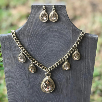 Gold chain necklace and matching teardrop crystal earrings displayed on gray wooden stand