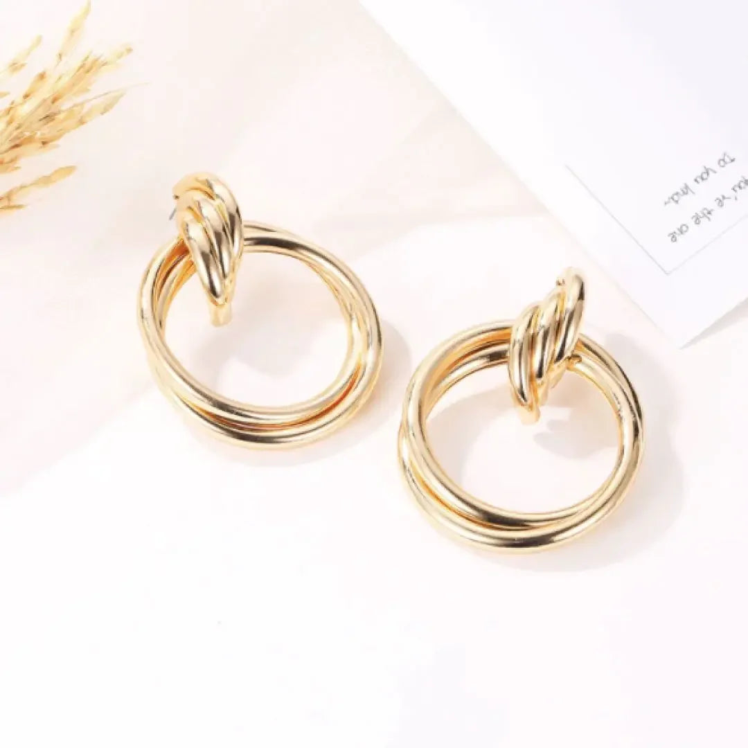 Pair of elegant gold hoop earrings with twisted top design on white surface