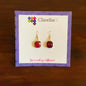 ClaudiaG red gemstone dangle earrings on branded card with purple border, displayed on wooden surface