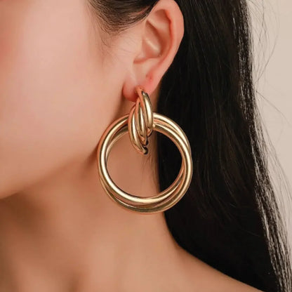 Close-up of a woman's ear wearing a large, polished gold hoop earring, elegant fine jewelry