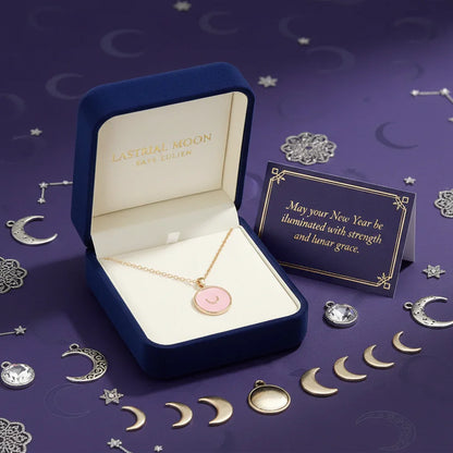Astral Moon gold pendant necklace with pink crescent moon charm in blue velvet box on purple lunar-themed background with a New Year message card