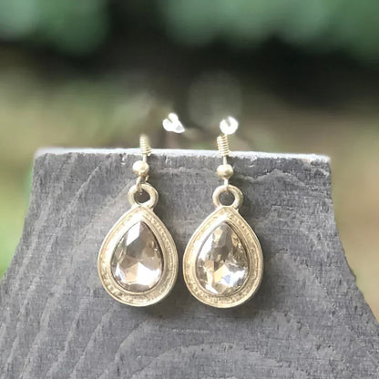 Pair of elegant teardrop-shaped gold earrings with faceted clear gemstones on rustic wooden display