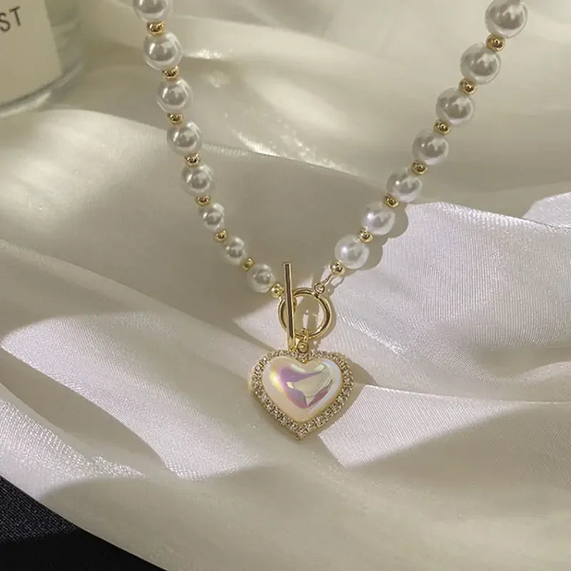 Pearl necklace with gold bead accents and heart-shaped pendant on white satin fabric
