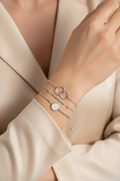 Elegant layered silver bracelets including linked rings and a disc charm on wrist in beige blazer