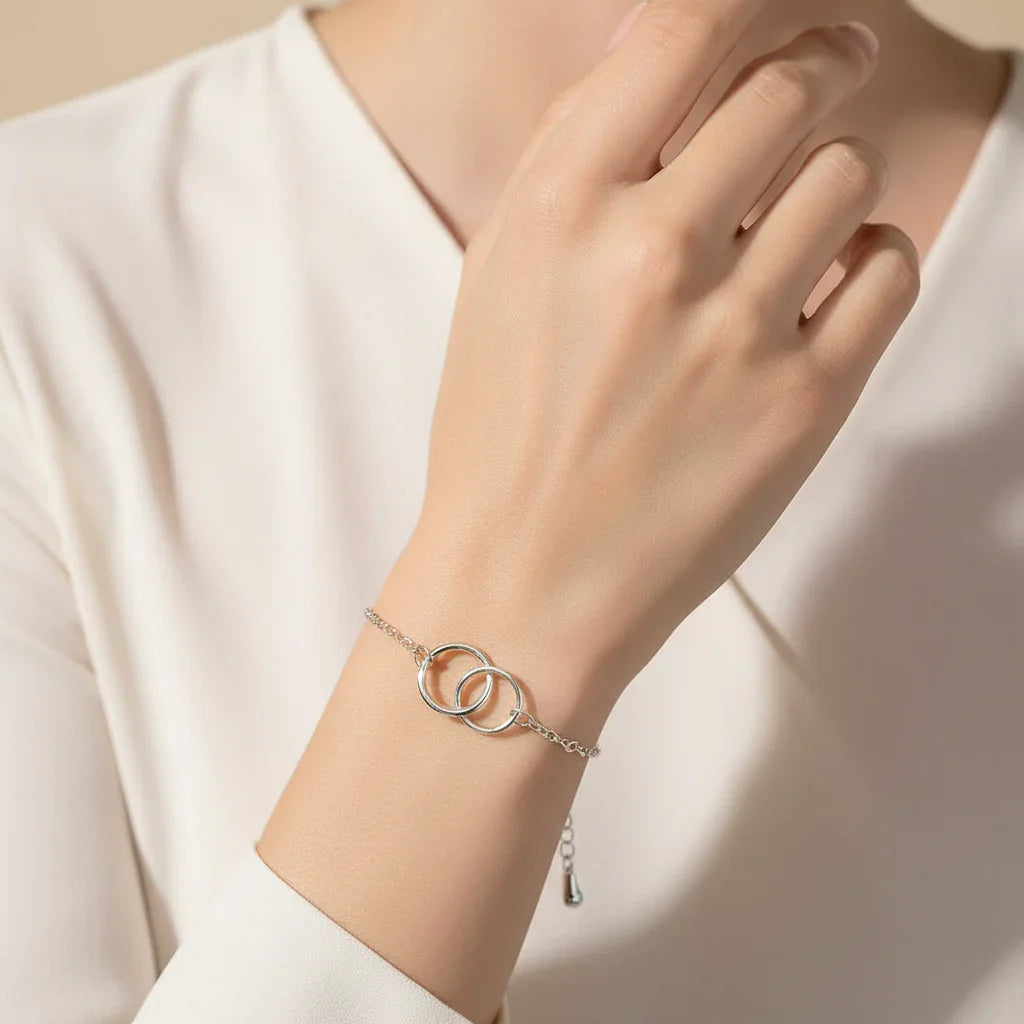 Elegant silver bracelet with two linked circles worn on wrist over ivory blouse