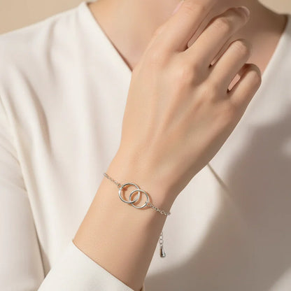 Elegant silver bracelet with two linked circles worn on wrist over ivory blouse