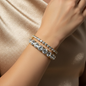 Close-up of a wrist wearing two gold crystal cuff bracelets on a champagne satin background