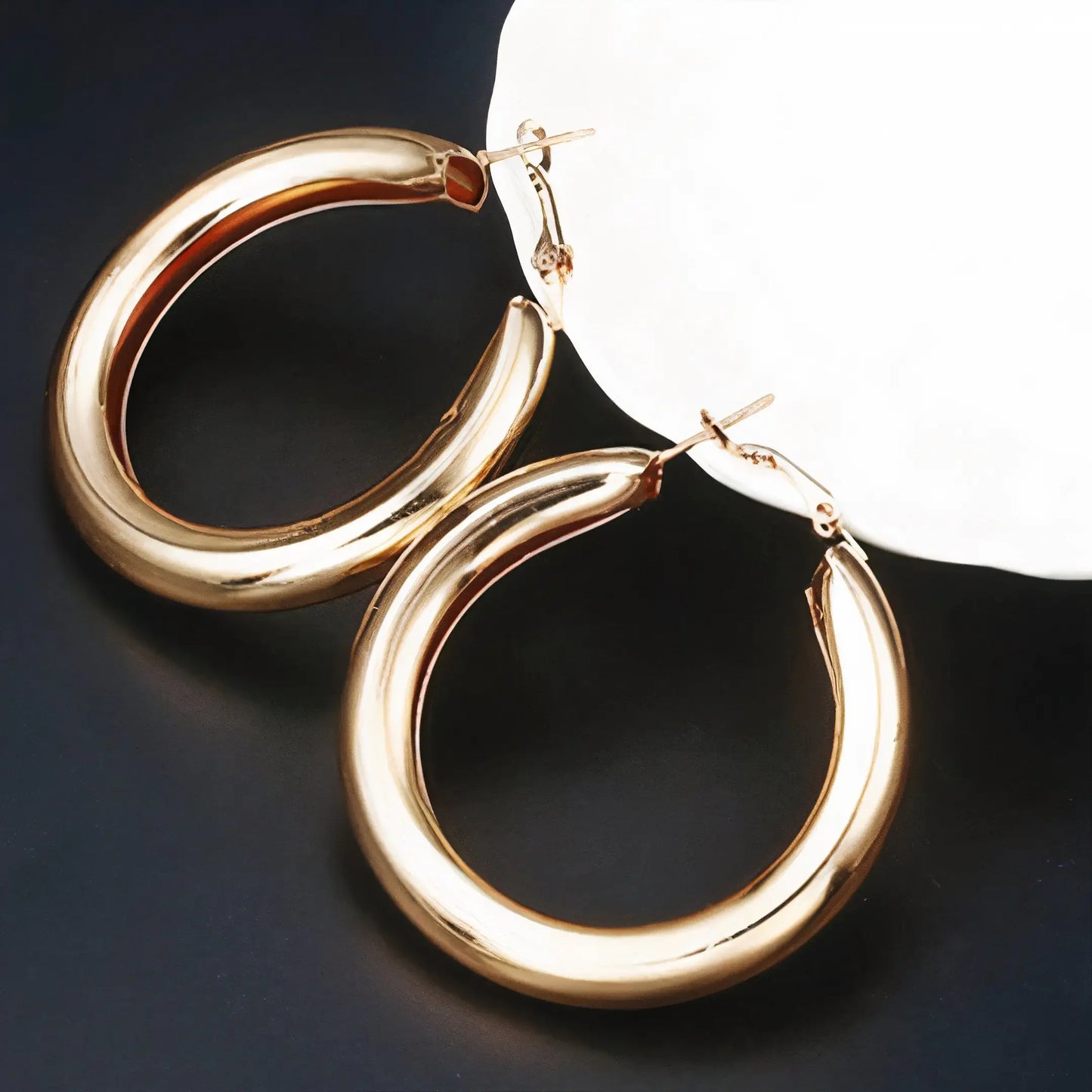 Pair of polished gold hoop earrings on black and white background, elegant everyday luxury jewelry