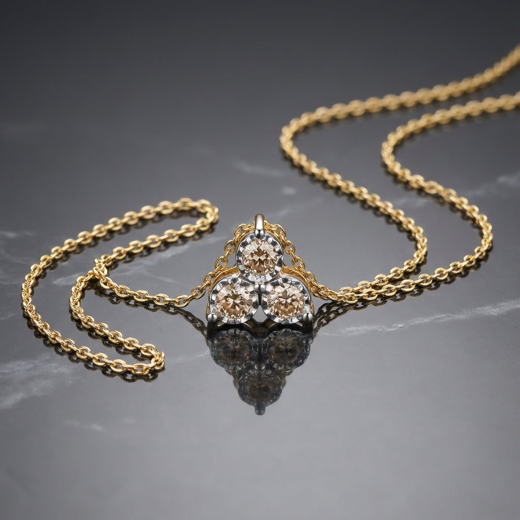Gold chain necklace with a pendant featuring three round beige diamonds on grey marble surface