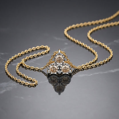 Gold chain necklace with a pendant featuring three round beige diamonds on grey marble surface