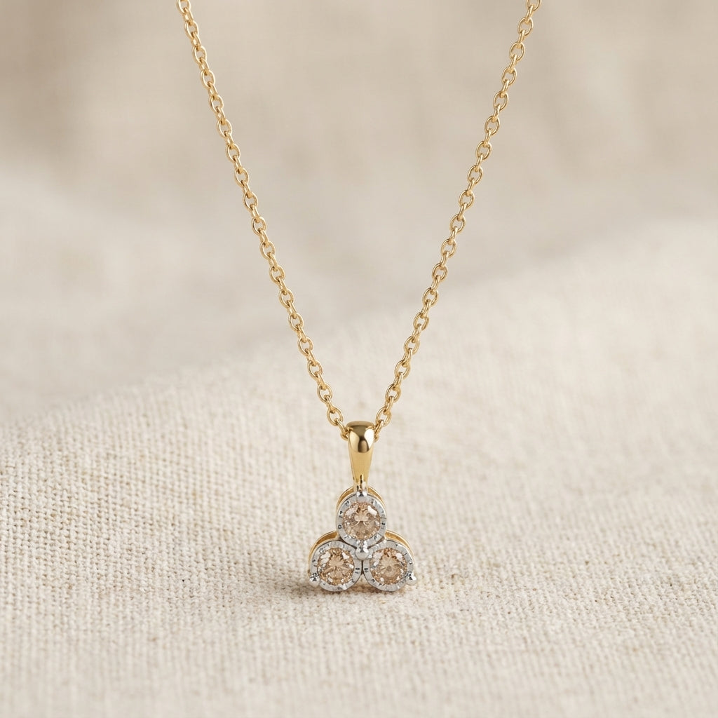 Gold chain necklace with a modern pendant featuring three round champagne gemstones on beige fabric