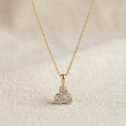 Gold chain necklace with a modern pendant featuring three round champagne gemstones on beige fabric