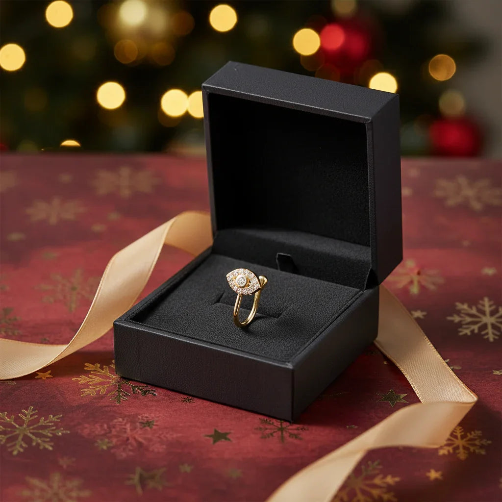 Gold eye-shaped ring with diamonds in black velvet gift box on red holiday wrapping paper with gold ribbon