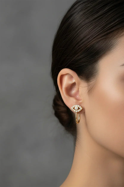 Close-up of woman's ear wearing a gold and diamond eye-shaped stud earring with a small gold hoop below
