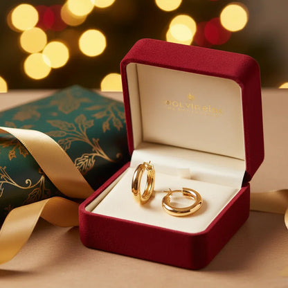 gold huggie earrings displayed in a red velvet jewelry gift box with festive bokeh lights and wrapped present