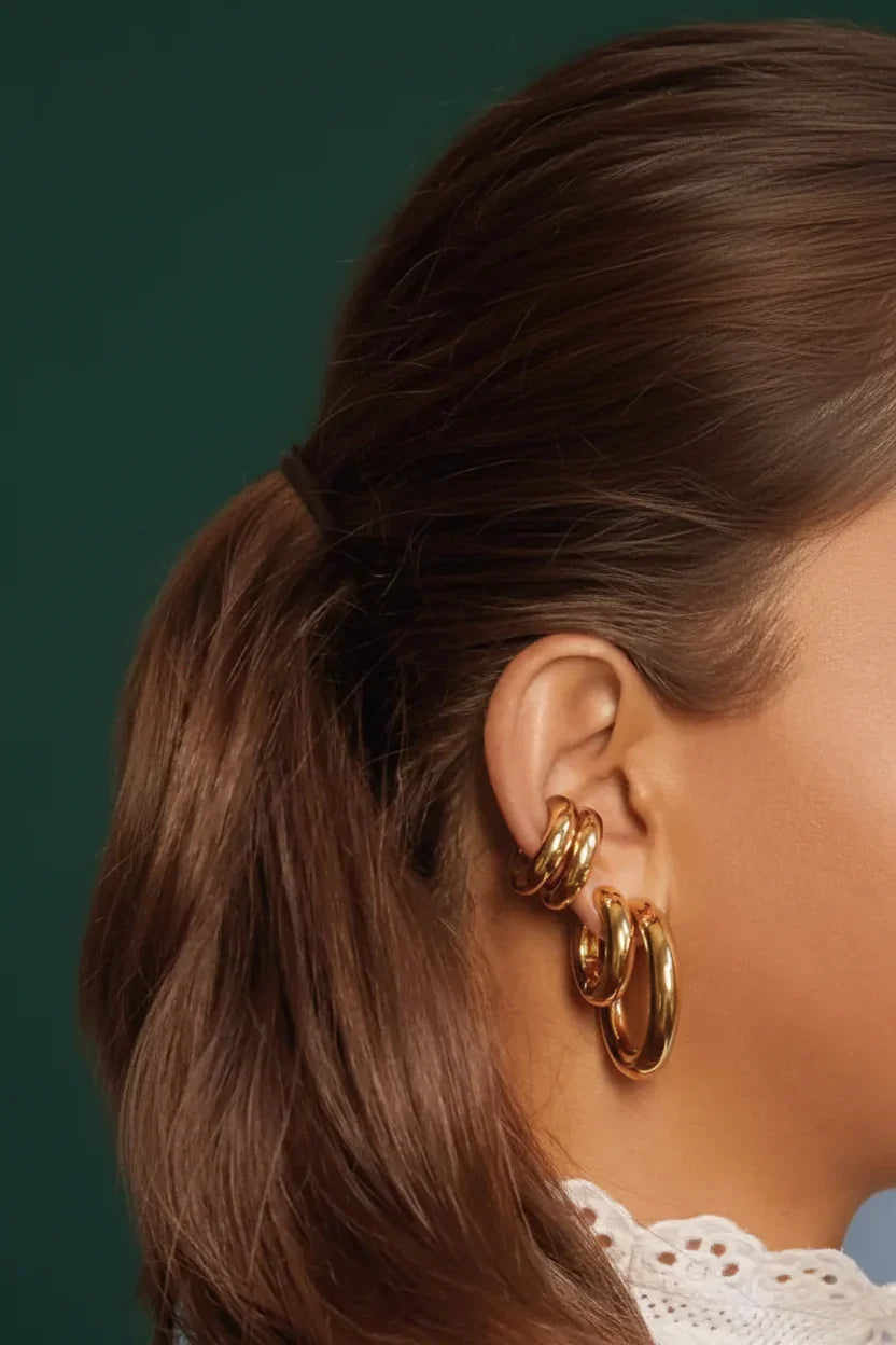 Close-up of a woman wearing stacked gold huggie hoop earrings with brown hair tied back, elegant jewelry