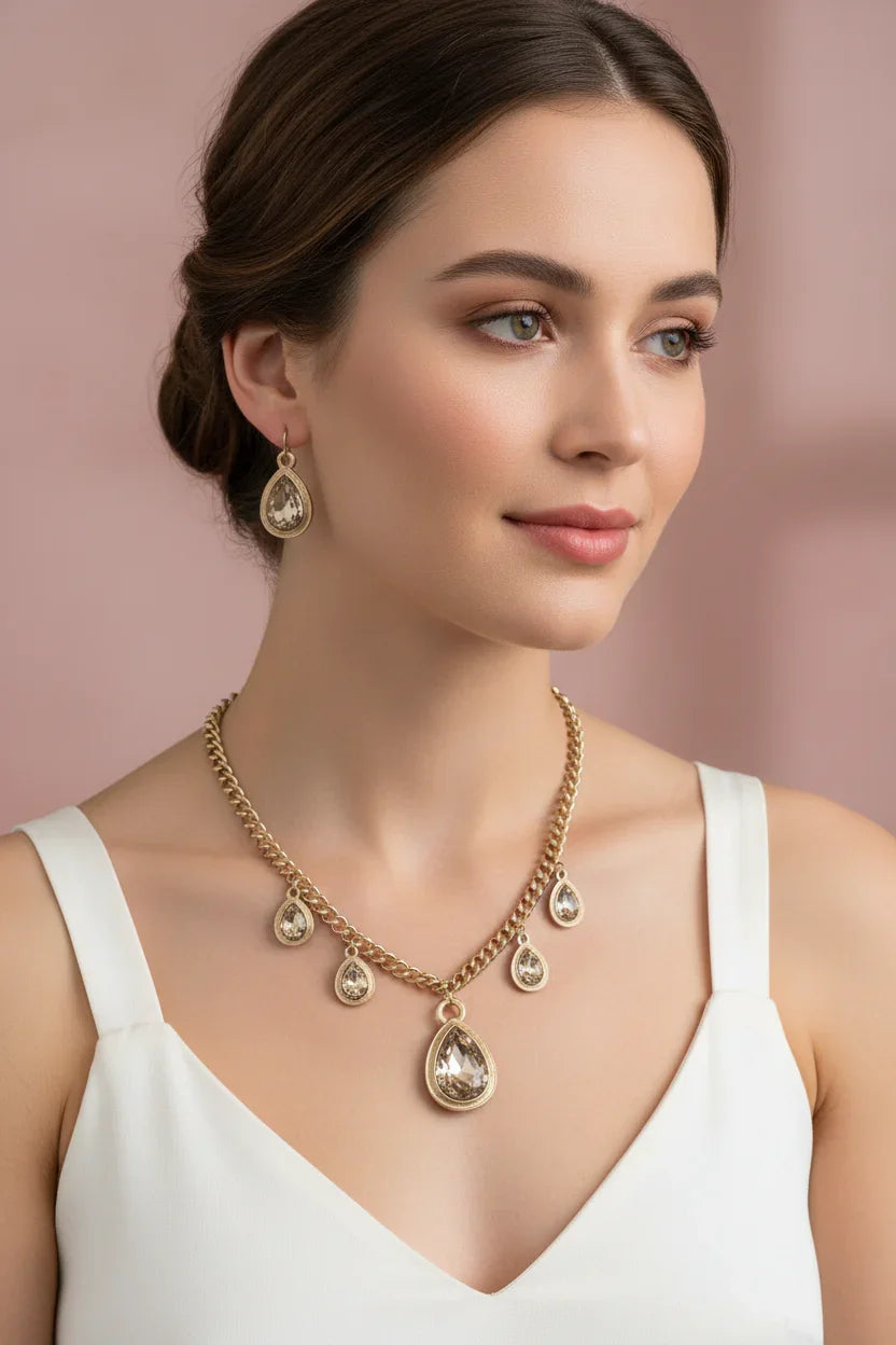 Woman wearing gold necklace and matching teardrop earrings with clear stones on a soft pink background
