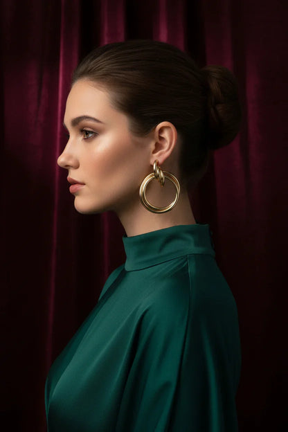 Profile of woman wearing elegant large gold statement hoop earrings and green high-neck gown against burgundy curtain