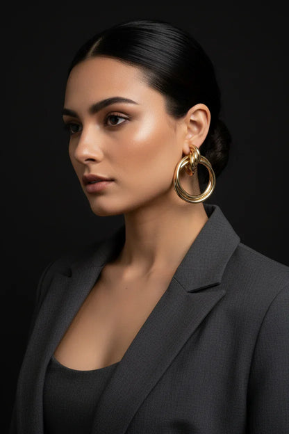 Profile of woman wearing modern gold statement hoop earrings and a dark blazer against black background
