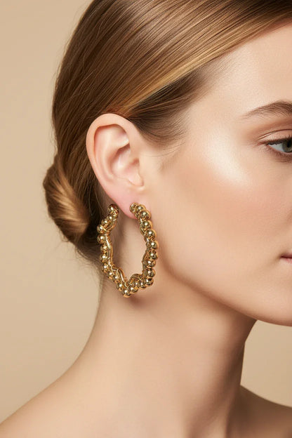 Close-up of woman wearing textured gold hoop earrings against champagne background
