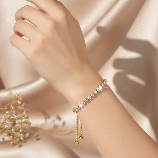 Hand wearing a gold vermeil bracelet with sparkling clear stones on a champagne satin background