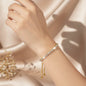 Hand wearing a gold vermeil bracelet with sparkling clear stones on a champagne satin background