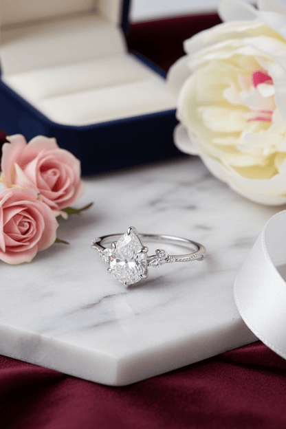 Elegant pear-shaped diamond engagement ring on marble with pink roses and white flower
