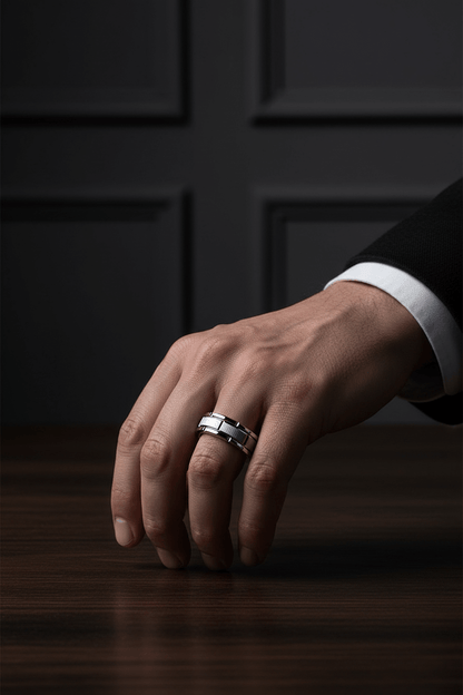 Close-up of a man's hand wearing a sleek tungsten ring on the ring finger against a dark paneled background
