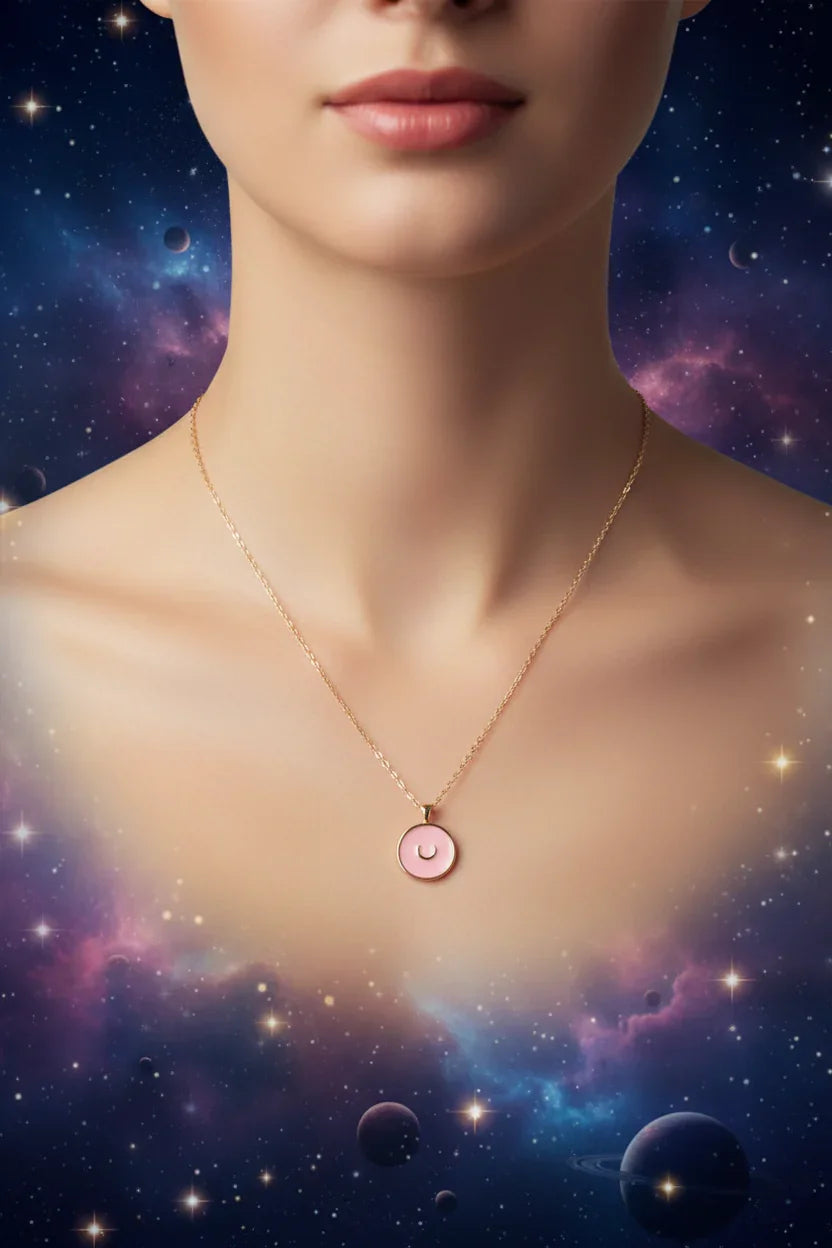 Close-up of a woman wearing a gold chain necklace with a pink moon pendant against a cosmic starry background