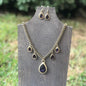 Gold-tone necklace and earrings set with teardrop-shaped dark purple gemstones on wooden display
