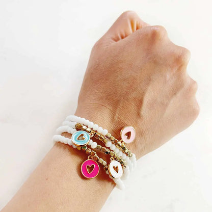 Hand wearing layered white beaded bracelets with gold and colorful heart charm accents