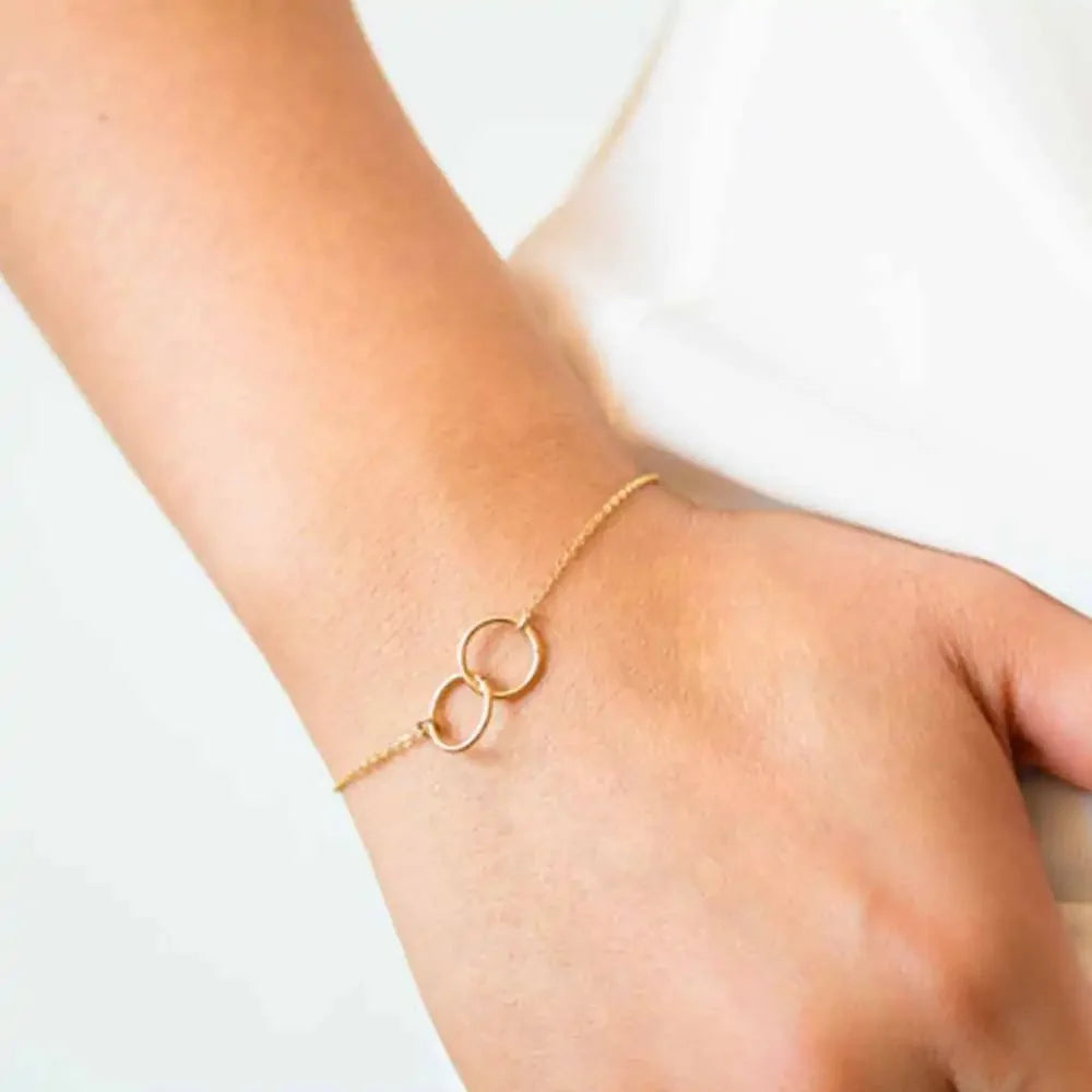 Delicate gold bracelet with two interlocking rings on wrist, minimalistic fine jewelry