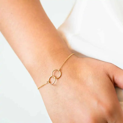 Delicate gold bracelet with two interlocking rings on wrist, minimalistic fine jewelry