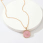 Delicate gold necklace with a round pink swirl pendant on white circular display, fine jewellery from Azure Jewelry