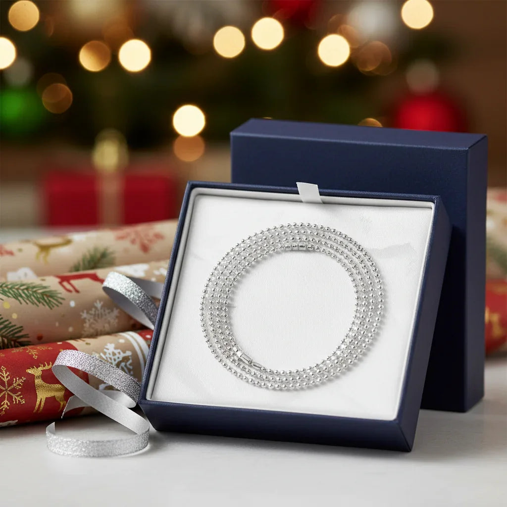 Silver beaded chain necklace in navy blue Christmas gift box with festive wrapping paper and bokeh lights