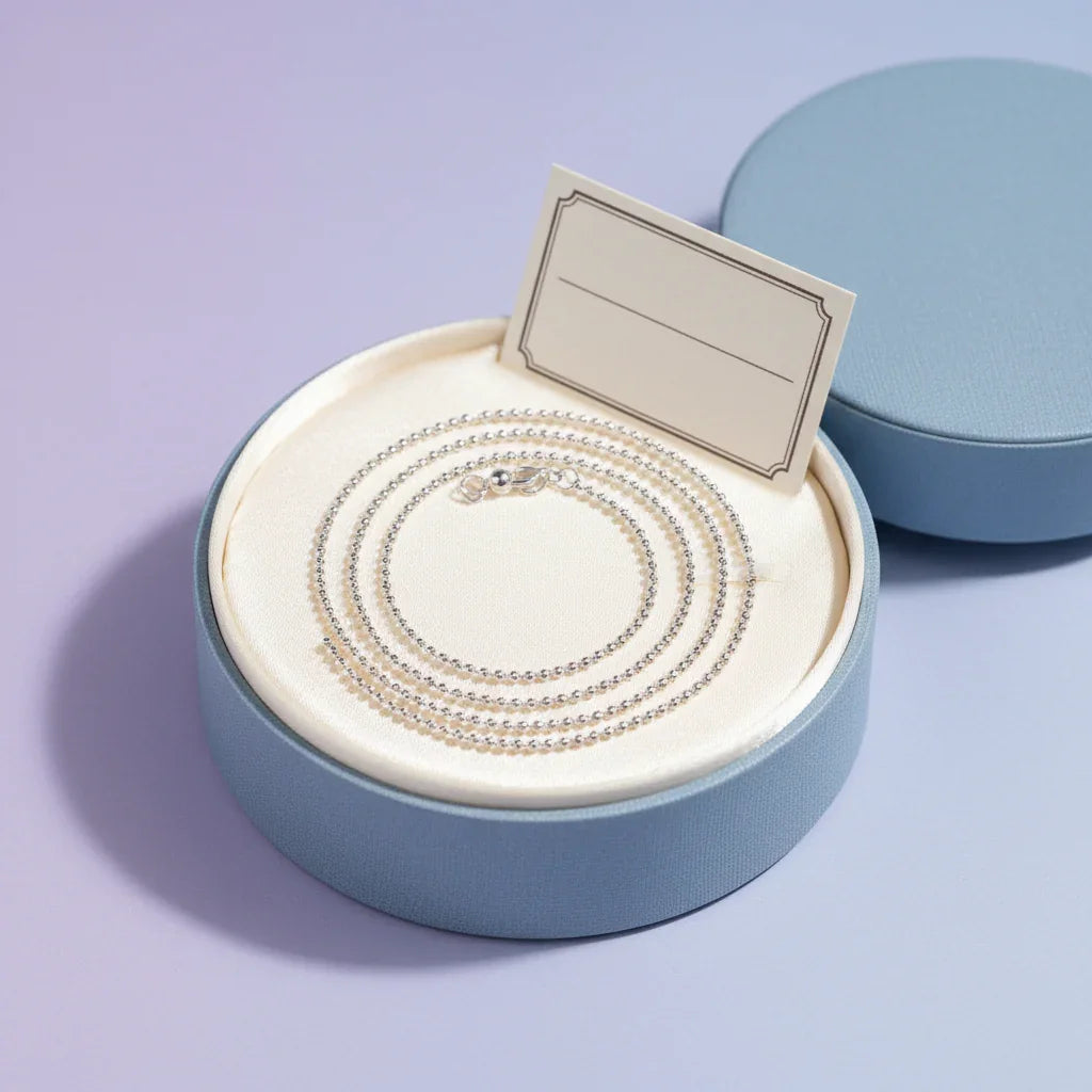 Elegant silver chain necklace displayed in a round blue gift box with cream interior and blank tag
