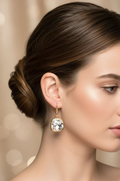 Elegant square crystal drop earrings with golden hooks worn by woman against champagne background