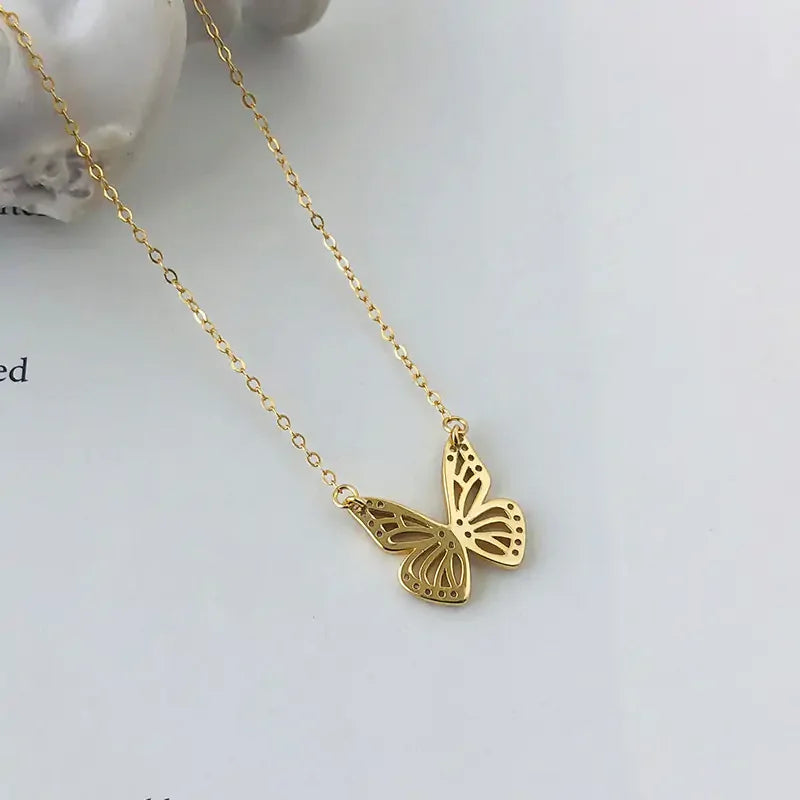 Delicate gold butterfly pendant necklace on fine chain, displayed on white surface with decorative background