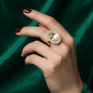 Hand with dark red nails wearing a vintage gold cocktail ring with a large oval crystal surrounded by pearls on green velvet background
