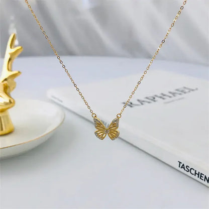 Delicate gold butterfly pendant necklace displayed with a gold deer figurine and a book on marble surface